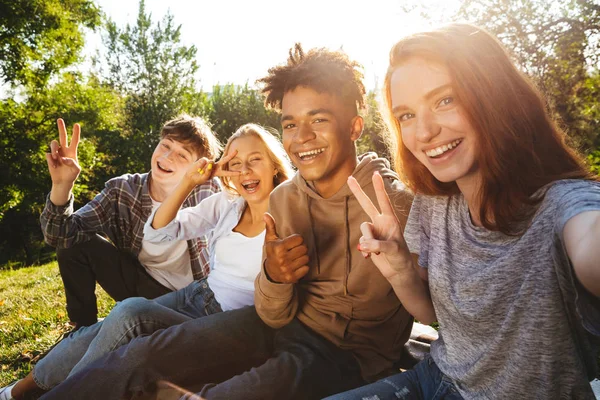 Grup birlikte sonra parkta, ödev heyecanlı multhiethnic öğrenci cep telefonu ile bir selfie alarak
