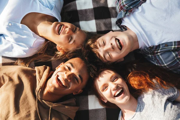 Portrait of happy people men and women laughing and lying on blanket in circle outdoor