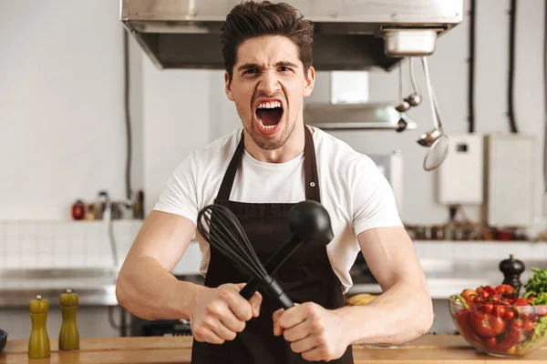 Chef Joven Enojado Cocinero Delantal Pie Cocina Sosteniendo Cucharón Batidor —  Fotos de Stock