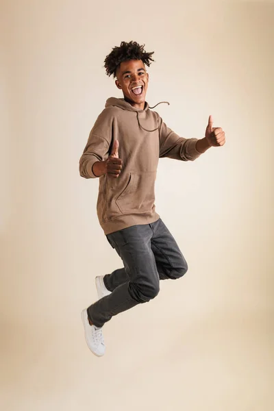 全长肖像的一个开朗的年轻美国黑人男子穿着帽衫跳跃孤立 显示竖起大拇指 — 图库照片
