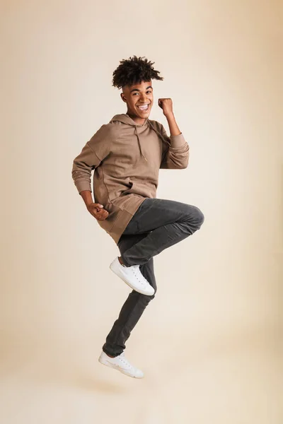 全长肖像一个兴奋的年轻美国黑人男子穿着帽衫跳跃孤立做赢家手势 — 图库照片
