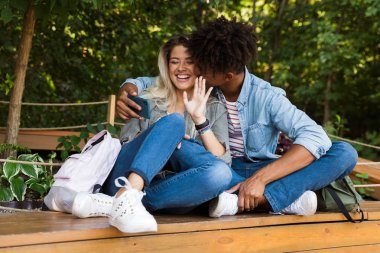 Konuşurken parkta birlikte vakit, bir selfie alarak, öpüşme genç çok ırklı çift heyecanlı