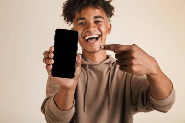 一个微笑的年轻美国黑人男子的肖像身着帽衫隔离 指向空白屏幕移动电话 — 图库照片