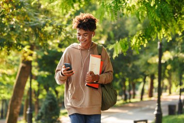 Sonra parkta, yürüyüş sırt çantası ile mutlu genç Afrika adam kulaklık ile müzik dinlemek