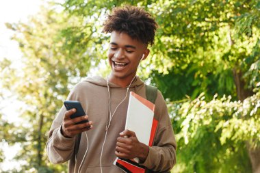 Sonra parkta, yürüyüş sırt çantası ile neşeli genç Afrika adam kulaklık ile müzik dinlemek