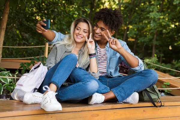 Excited young multiethnic couple talking while spending time together at the park, taking a selfie