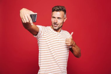 Kırmızı arka plan üzerinde duran, bir selfie alarak, başparmak gösterilmesini neşeli bir adam portresi