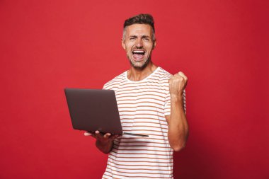 Görüntü gülümseyen ve gri laptop izole kırmızı arka plan üzerinde tutarak çizgili tişört başarılı biri