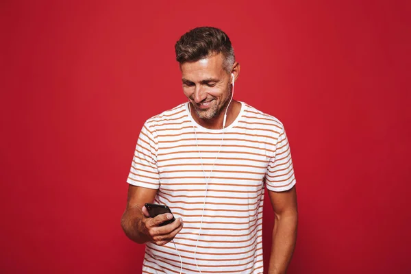 Portret Van Een Glimlachende Man Permanent Rode Achtergrond Luisteren Naar — Stockfoto