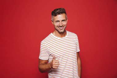 Gülümseyen ve başparmak kırmızı arka plan üzerinde izole gösterilmesini çizgili tişört çekici adam