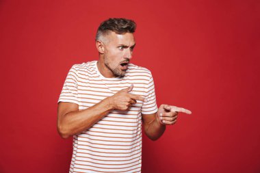 Şok yetişkin adam 30'lu yaşlarda bir kenara boşaltmak izole kırmızı arka plan üzerinde işaret parmağı portresi