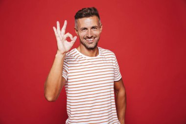 Gülümseyen ve ok işareti izole kırmızı arka plan üzerinde gösterilen çizgili tişört esmer genç adam