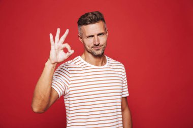 Yakışıklı adam 30'lu gülümseyen ve ok işareti izole kırmızı arka plan üzerinde gösterilen çizgili tişört
