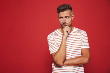 Düşünme ve kırmızı arka plan üzerinde izole çene dokunmadan çizgili tişört tıraşsız adam