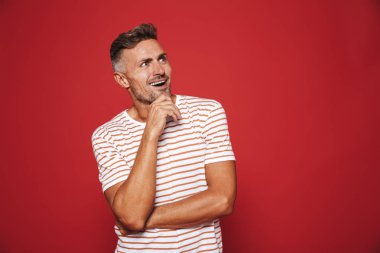 Çene dokunmadan ve boşaltmak izole kırmızı arka plan üzerinde bir kenara bakarak çizgili tişört tıraşsız adam