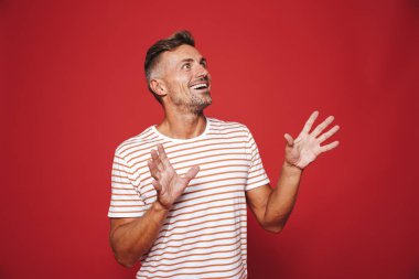 Esmer adam seviniyor ve boşaltmak izole kırmızı arka plan üzerinde bir kenara bakarak çizgili tişört
