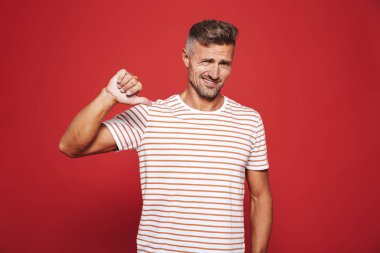 Başparmak aşağı gösterilen ve kırmızı arka plan üzerinde izole sevmediğim ifade çizgili tişört hayal kırıklığına adam