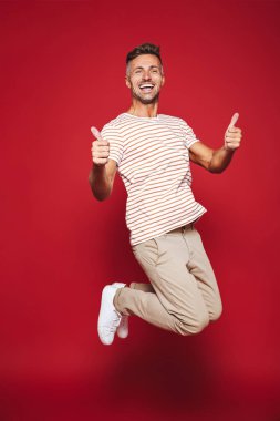 Atlama ve başparmak kırmızı arka plan üzerinde izole gösterilmesini çizgili tişört beyaz adamın tam uzunlukta fotoğraf