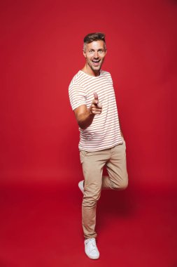 Tam uzunlukta fotoğraf gülümseyen ve başparmak kırmızı arka plan üzerinde izole gösterilmesini çizgili tişört tıraşsız insanın