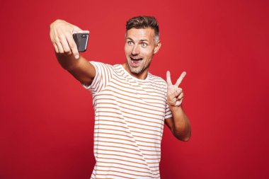 Kırmızı arka plan üzerinde duran, bir selfie alarak neşeli bir adam portresi