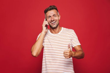 Kırmızı arka plan üzerinde duran, cep telefonu üzerinde konuşurken gülümseyen bir adam portresi