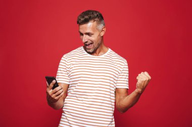 Kırmızı arka plan üzerinde duran, cep telefonu seyir gülümseyen bir adam portresi