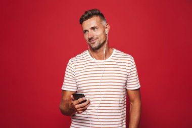 Cep telefonu tutan kulaklık ile müzik dinlemek kırmızı arka plan üzerinde duran mutlu bir adam portresi
