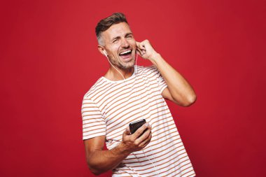 Cep telefonu, dans holding ile kulaklık, müzik dinlemek kırmızı arka plan üzerinde duran gülümseyen bir adam portresi
