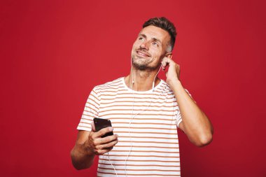 Kulaklık ile müzik dinlemek, cep telefonu tutan, ararken kırmızı arka plan üzerinde duran bir gülümseyen adam portresi
