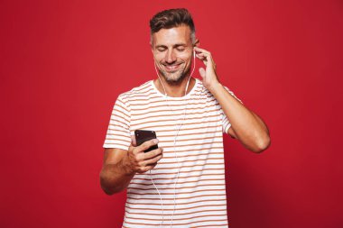 Cep telefonu tutan kulaklık ile müzik dinlemek kırmızı arka plan üzerinde duran gülümseyen bir adam portresi