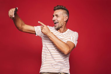 Bir selfie alarak kırmızı arka plan üzerinde ayakta neşeli bir adam portresi işaret