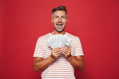Görüntü gülümseyen ve izole kırmızı arka plan üzerinde para banknot hayranı tutan çizgili tişört heyecanlı adamın
