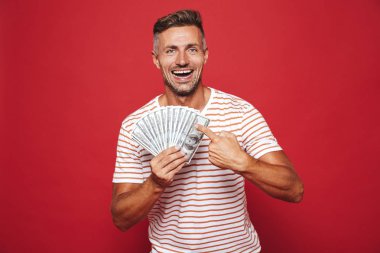 Görüntü gülümseyen ve izole kırmızı arka plan üzerinde para banknot hayranı tutan çizgili tişört yakışıklı adamın