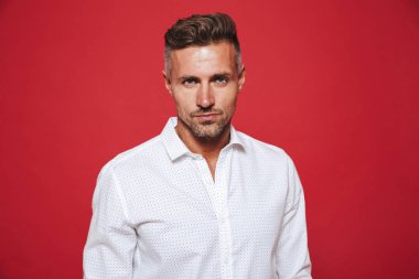 Yakışıklı esmer 30'lu yaşlarda olan adam anız beyaz gömlek kırmızı arka plan üzerinde izole kamera üzerinde seyir