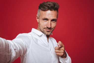 Beyaz esmer 30'lu yaşlarda olan adam anız el hareketi ve selfie fotoğrafta izole kırmızı arka plan üzerinde beyaz gömlekli