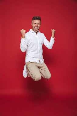 Tam uzunlukta fotoğraf başarılı erkeğin atlama ve kırmızı arka plan üzerinde izole yumruk kenetlenmesi formal giyim