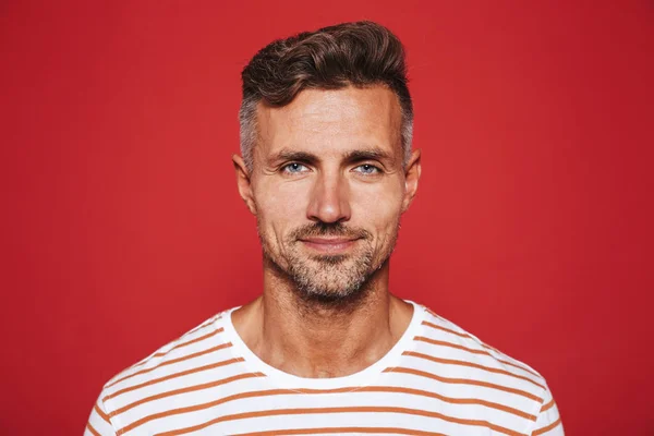 Adult attractive man with stubble in striped t-shirt smiling on camera isolated over red background