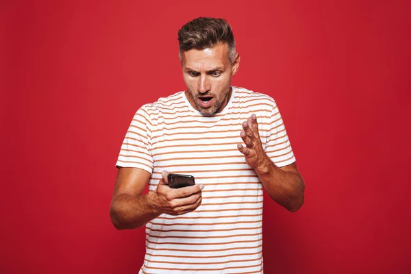 Retrato Hombre Sorprendido Pie Sobre Fondo Rojo Mirando Teléfono Móvil — Foto de Stock