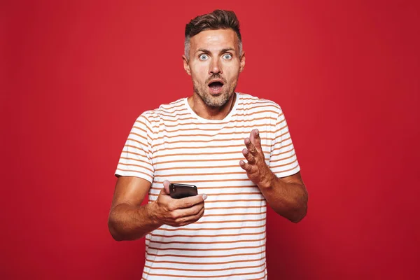 Porträtt Upphetsad Man Står Över Röd Bakgrund Tittar Mobiltelefon — Stockfoto