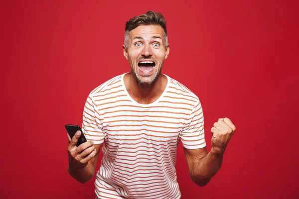 Портрет Взволнованного Человека Стоящего Красном Фоне Держащего Мобильный Телефон Празднующего — стоковое фото