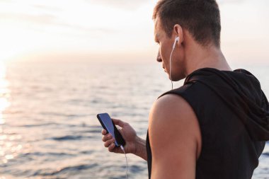 Yakışıklı güçlü genç sporcu beach kulaklık ile müzik dinleme, açık havada resim.