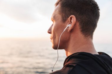 Yakışıklı güçlü genç sporcu beach kulaklık ile müzik dinleme, açık havada resim.