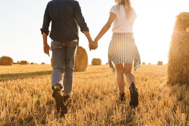 Adam ve kız güneşli gün boyunca altın alan haystacks grup ile el ele yürürken fotoğrafı kırpılmış