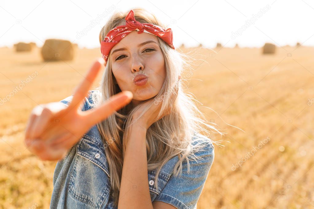 Beautiful lovely young blonde girl in headband at the wheat field, showing peace sign