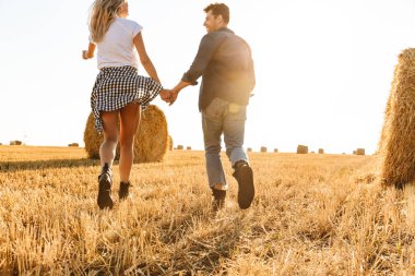 Romantik Çift erkek ve kadın haystacks grup ile altın alan aracılığıyla güneşli gün boyunca yürüyüş yaparken eğlenmek fotoğraf