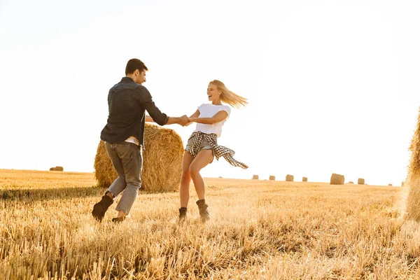 うれしそうなカップル男女晴れた日の間に干し草の束を持つゴールデン フィールドを歩きながら楽しんでの写真 — ストック写真