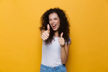 Görüntü gülümseyen ve başparmak sarı arka plan üzerinde izole gösterilmesini kıvırcık saçlı olumlu kadının 20'li