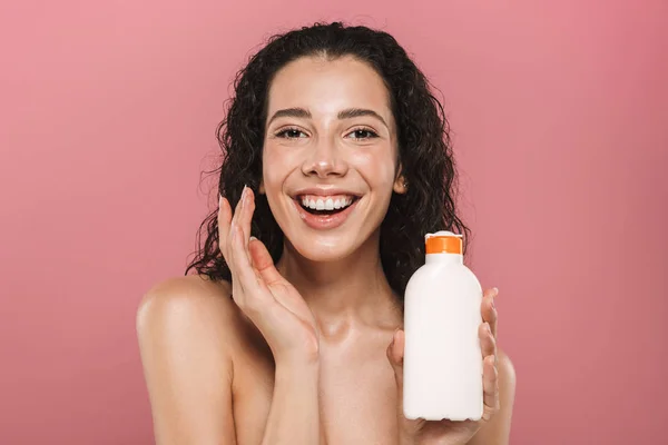 クリーム化粧水ゲルを保持彼女の肌の世話をするピンク背景に分離されたポーズ幸せ笑顔の美しい若い女性の肖像画 — ストック写真