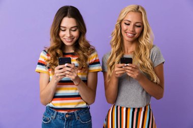 İki güzel menekşe arka plan üzerinde izole duran genç kız arkadaşlar cep telefonunu kullanarak gülümseyen