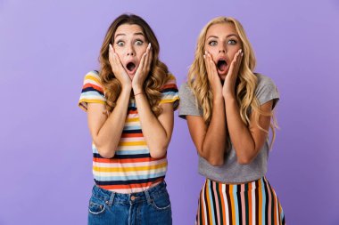 Menekşe arka plan üzerinde izole duran iki oldukça şok genç kız arkadaş çığlık